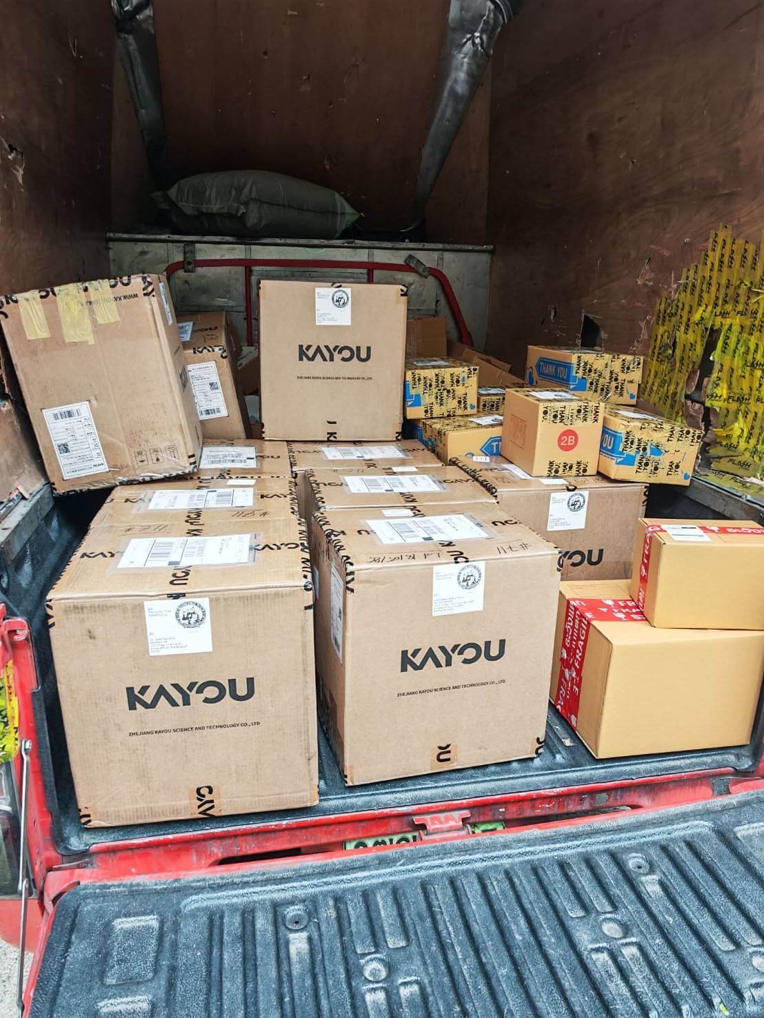 Multiple cardboard boxes printed with the brand name KAYOU stacked inside the back of a red truck.